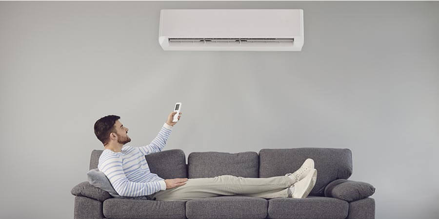 man relaxing on sofa holding remote and controlling a ductless ac unit on the wall